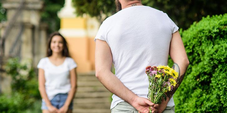 Man hides flower bouquet behind back while waits girl romantic date. First impression always important. Surprise for her. Couple meeting for date park background. Guy prepared surprise for girlfriend