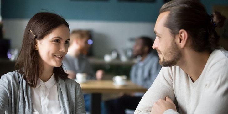 Happy millennial couple in love talking sitting at coffee house table together, smiling young attractive man and woman chatting and flirting enjoying pleasant conversation, date in cafe concept