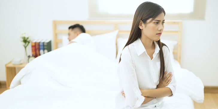 Young couple in the bedroom, the woman is sitting alone and crying, relationship difficulties concept