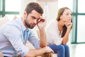 Relationship breakdown. Depressed young man holding hand on head and looking away while woman sitting behind him on the couch