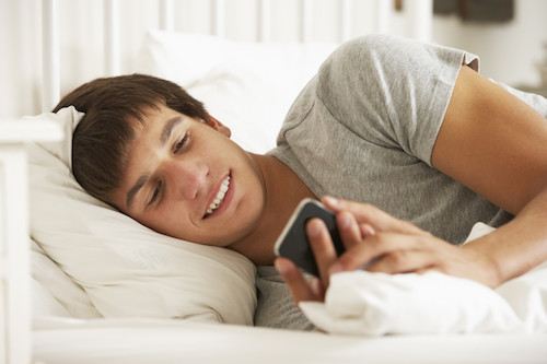 Teenage Boy In Bed At Home Texting On Mobile Phone