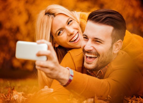 Happy couple lying in the park among leaves,enjoying in the beautiful autumn day.