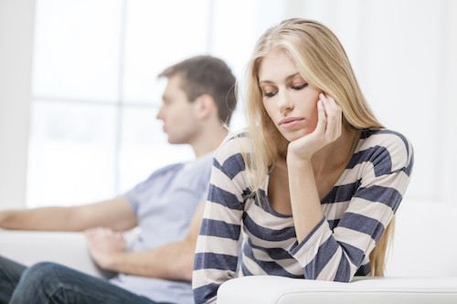 Upset young woman sitting with her husband in the background